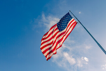 American USA flag on a flagpole waving in the wind. USA Flag Waving United States of America Flag Flying. American flag flying high on a pole against blue sky background on a clear day
