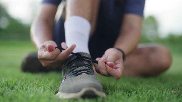 Asian man in sportswear tying running shoelaces during jogging exercise at public park in summer morning. Healthy guy athlete enjoy outdoor lifestyle sport training fitness workout running in the city