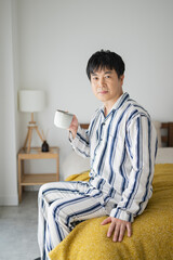 Fototapeta premium 朝、ベッドでコーヒーを飲む50代男性