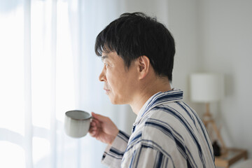 朝、ベッドでコーヒーを飲む50代男性