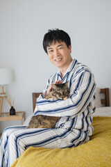 ベッドに座って猫を抱くパジャマ姿の50代男性