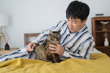 目が覚めてベッドで猫と戯れる50代男性