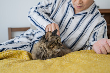 目が覚めてベッドで猫と戯れる50代男性