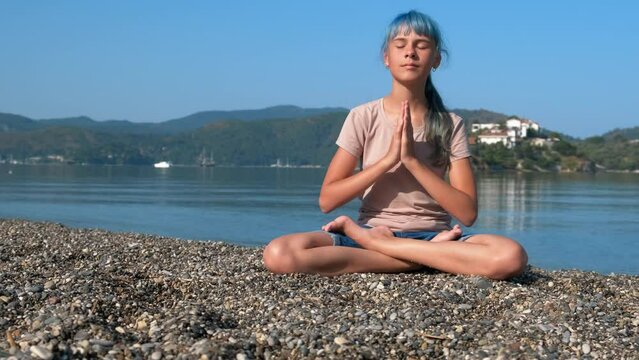 Namaste pose against seascape. A smart pensive girl sitting in namaste pose against morning seascape in summer.