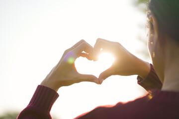 Happy - romantic couple making a hands gesture into heart shape together in a beautiful sunlight in morning in background. Happy healthy lifestyle concept.