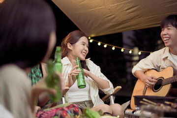 Group of diverse ethnicity young people enjoy eating and grilling bar-b-q together while camping in forest at night.