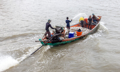 Asian fishermen sail on a boat full of caught fish