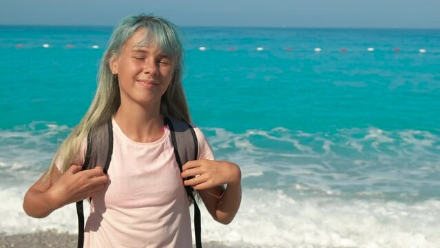 Stay on white beach under sun. A happy teen girl waving her blue hair against foaming blue sea on the luxury beach.