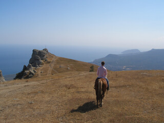 Man on horseback strolling on the Demerdzhi mountain plateau against the background of the southern coast of Crimea, Black Sea, Ayudag Mountain in the haze, horseback travel