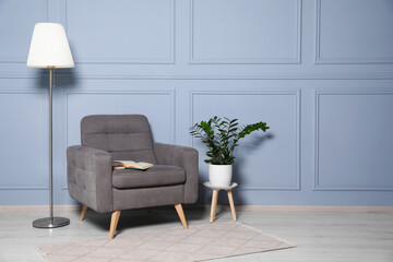 Cosy armchair, floor lamp and potted plant near light grey wall in room, space for text. Interior design