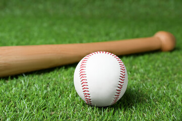 Obraz na płótnie Canvas Wooden baseball bat and ball on green grass. Sports equipment