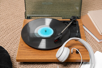 Stylish turntable with vinyl disc and headphones on carpet at home