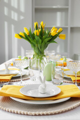 Fototapeta na wymiar Festive table setting with glasses, painted eggs and vase of tulips. Easter celebration