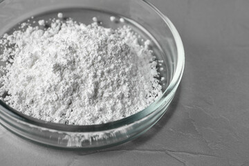 Petri dish with calcium carbonate powder on grey table, closeup
