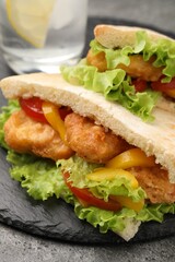 Delicious pita sandwiches with fried fish, pepper, tomatoes and lettuce on dark grey table, closeup