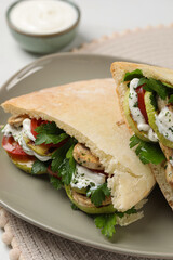 Delicious pita sandwiches with grilled vegetables and sour cream sauce on table, closeup