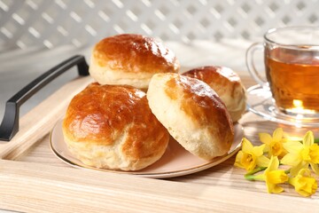 Freshly baked soda water scones, cup of tea and daffodils on wooden tray, closeup