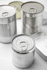 Many closed tin cans on white tiled table, closeup