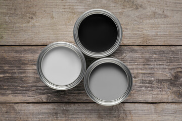 Cans of white, black and grey paints on wooden table, flat lay