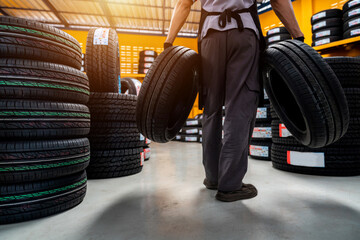 Naklejka na ściany i meble A male auto mechanic holding two tires in tire shop for storage or new tire stock at large warehouse at service center or auto repair shop for automotive industry. car industry.
