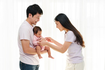 Fototapeta premium cheerful father and mother holding and playing with newborn baby on window background. happy family concept