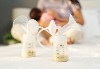 the breast milk are in the bottles of electric breast pumping set on bed with mother breastfeeding newborm baby background