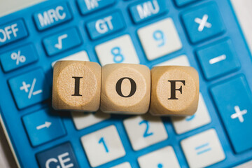 A sigla IOF para Imposto sobre operações financeiras escrita em dados de madeira que estão sobre uma calculadora azul. Economia Brasileira.
 - obrazy, fototapety, plakaty