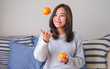 Portrait image of a young woman having fun while juggling oranges at home