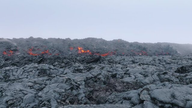 Drone flying to steaming black lava rocks. Red hot molten lava flowing through streams on slope. Lava flow on Big Island in Hawaii USA shot. Volcano eruption on Mauna Loa mountain 4K footage America