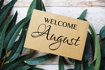 Welcome August text message top view on wooden background with green leaf decoration - obrazy, fototapety, plakaty