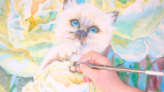 the artist man with a brush draws to a white cat with blue eyes smiles looks into frame the master's hand painting drawing flowers Bright delightful beauty on the wall decoration art