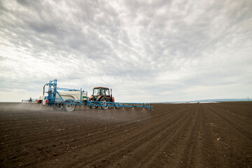 Obraz premium Tractor spraying pesticides on field with a sprayer