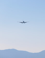 Fototapeta na wymiar View of modern passenger plane aircraft in flight, commercial airplane flying in the sky before take off or landing, with mountains in the background in a summer sunny day