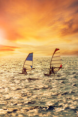 two man playing wind surf over rushing sea against beautiful sunset lighting