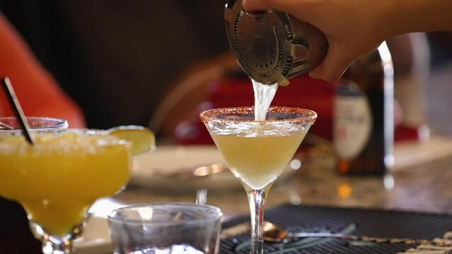 Bartender pours Mexican martini from shaker into a dressed glass, slow motion 4K