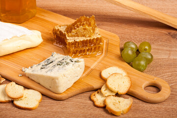 Delicious cheese plate with crackers, honey and grape on wooden background