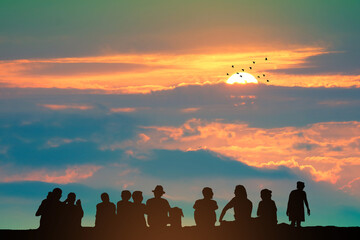 Fototapeta premium Silhouette people sitting on the top mountain and sunset on the colorful sky orange cloud and birds flying