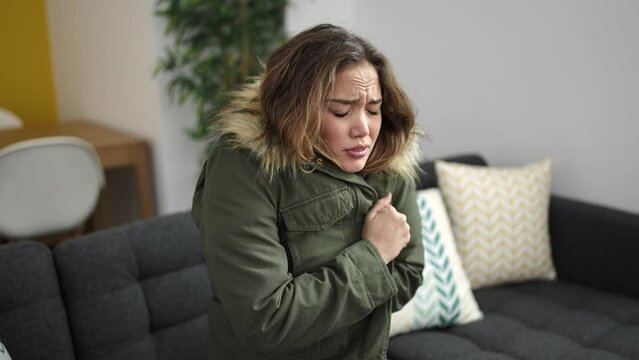 Young beautiful hispanic woman covering with jacket for cold rubbing hands at home