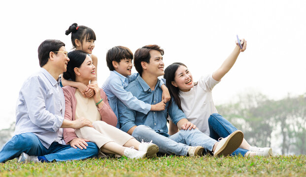 Image Of An Asian Family Sitting Together On The Grass At The Park