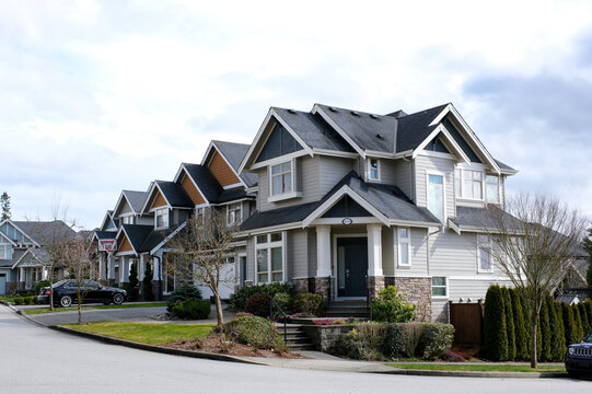 A row of a new houses in Surrey British Columbia, Canada. Front yards of the houses and street with trees and bushes. High quality photo