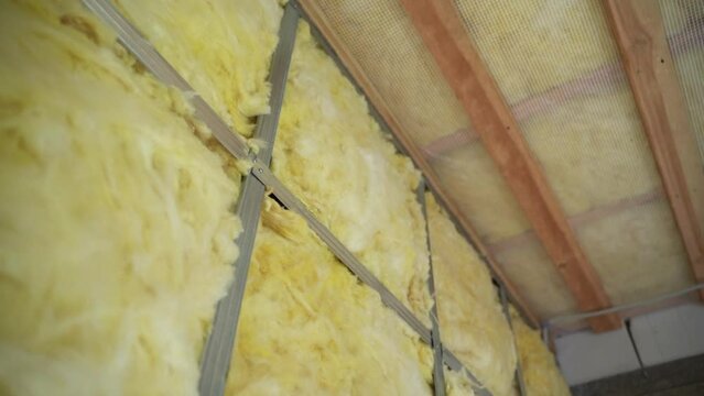 The use of glass wool for roof insulation and wall soundproofing, smooth camera movement. Private house with bare walls without interior renovation