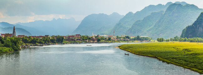 Panorama view of a wide river flowing past a village towards high mountains at Phong Nha in Vietnam