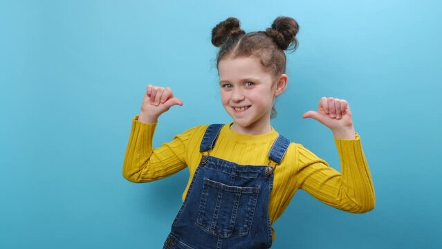 Portrait of happy adorable little kid girl pointing thumbs on herself, looking at camera, posing isolated over blue color background wall in studio. Childhood lifestyle and people emotion concept