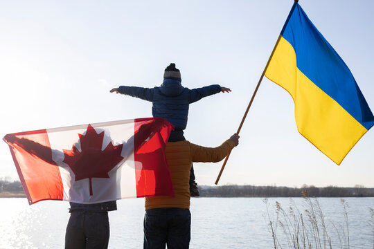 Family With A Child With Ukrainian And Canadian Flags Stand Together In Nature. International Support And Assistance To Ukraine, Stop The War With Russia. Problems Of Refugees And Immigrants