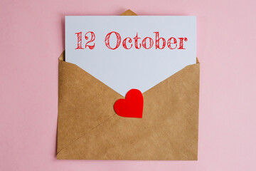 Kraft envelope with a white sheet of paper and a date 12 october, with a red heart. Flat lay on pink background, romance and love concept