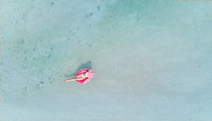 Aerial view with woman in bikini sunbathing as laying on swim ring  as blue sea water in background