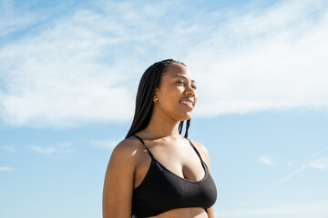 young black girl smiling relaxed on the beach, woman enjoying good spring summer weather wearing sportswear	