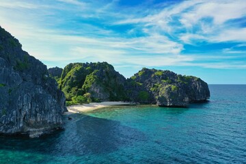Panorama drone shot of the paradisiacal beach of Coron, Palawan in the Philippines with fine white beach, palm trees and majestic rocks.