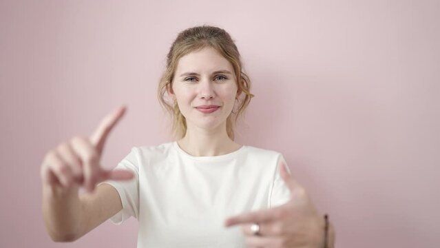 Young blonde woman smiling confident doing photo gesture with hands over isolated pink background