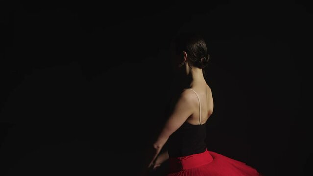 Ballerina dances in a red tutu in a dark room in the light of a sapphite. A symbol of elegance, grace and mobility. High quality 4k footage